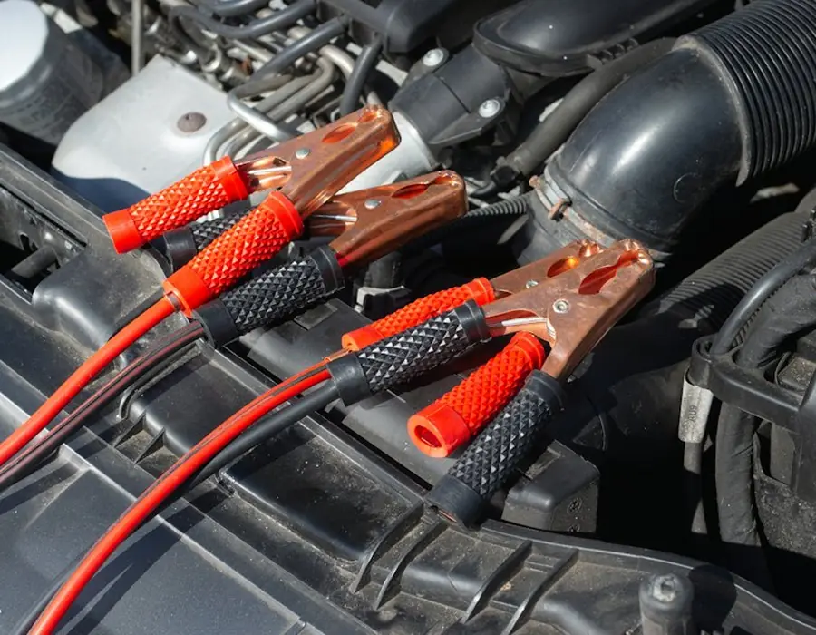 Jumper cables clamped to a car battery under an open bonnet
